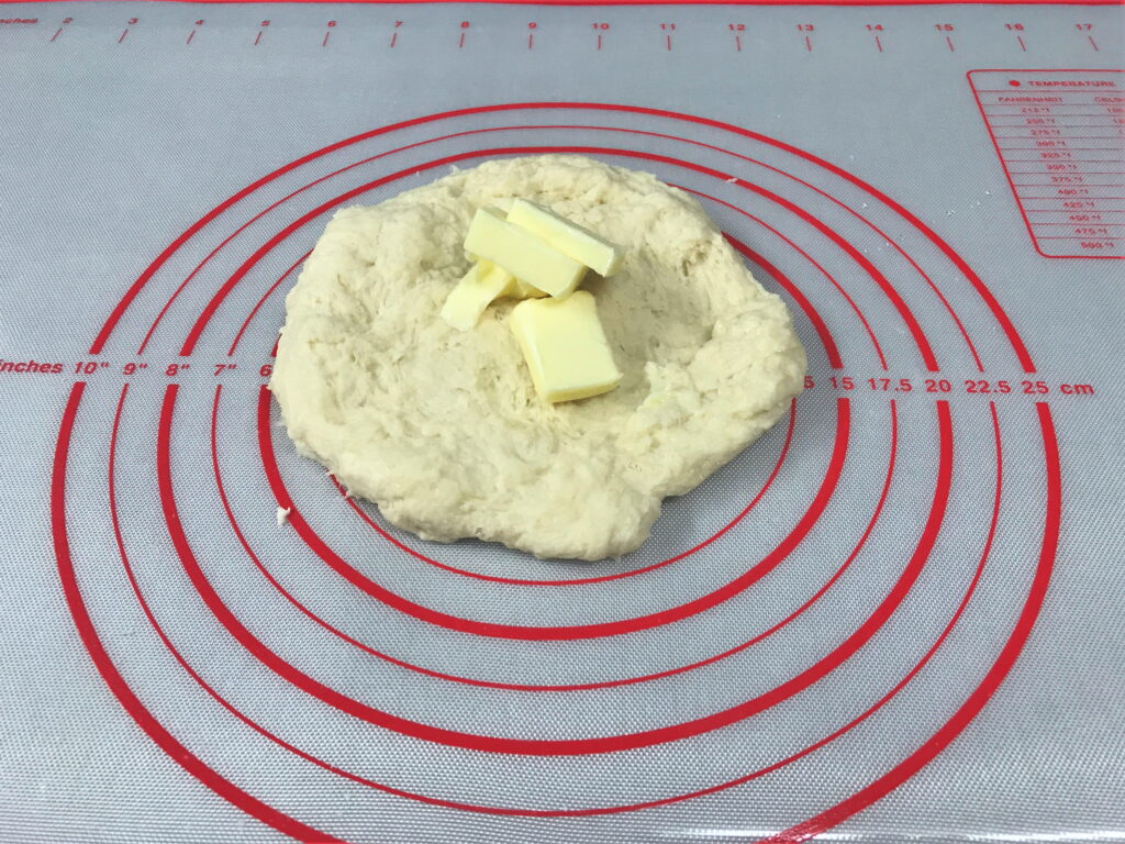 まとまってきたパン生地を広げてバターを乗せる