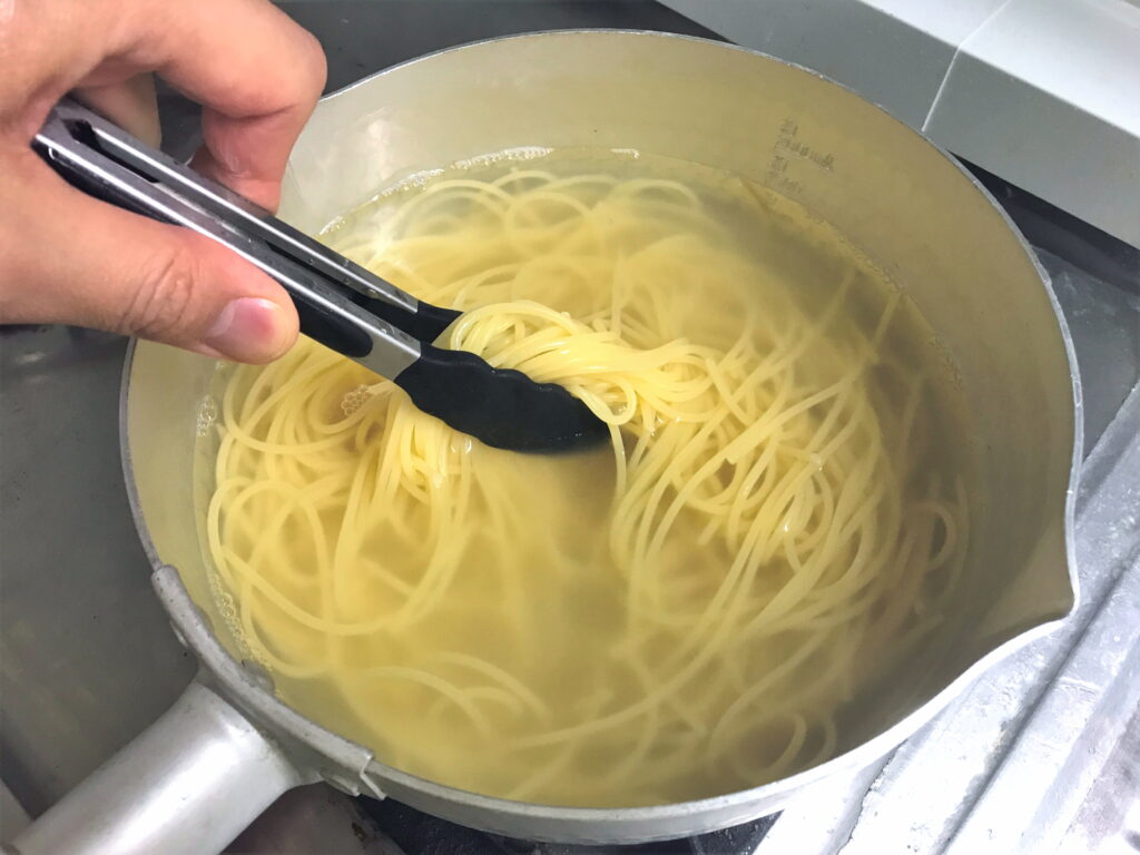 アルミ鍋で茹でたスパゲッティをトングでつかむ