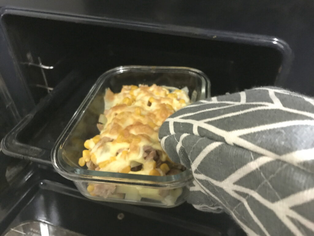 オーブンで焼いたポテトとツナとコーンのチーズ焼きを取り出す