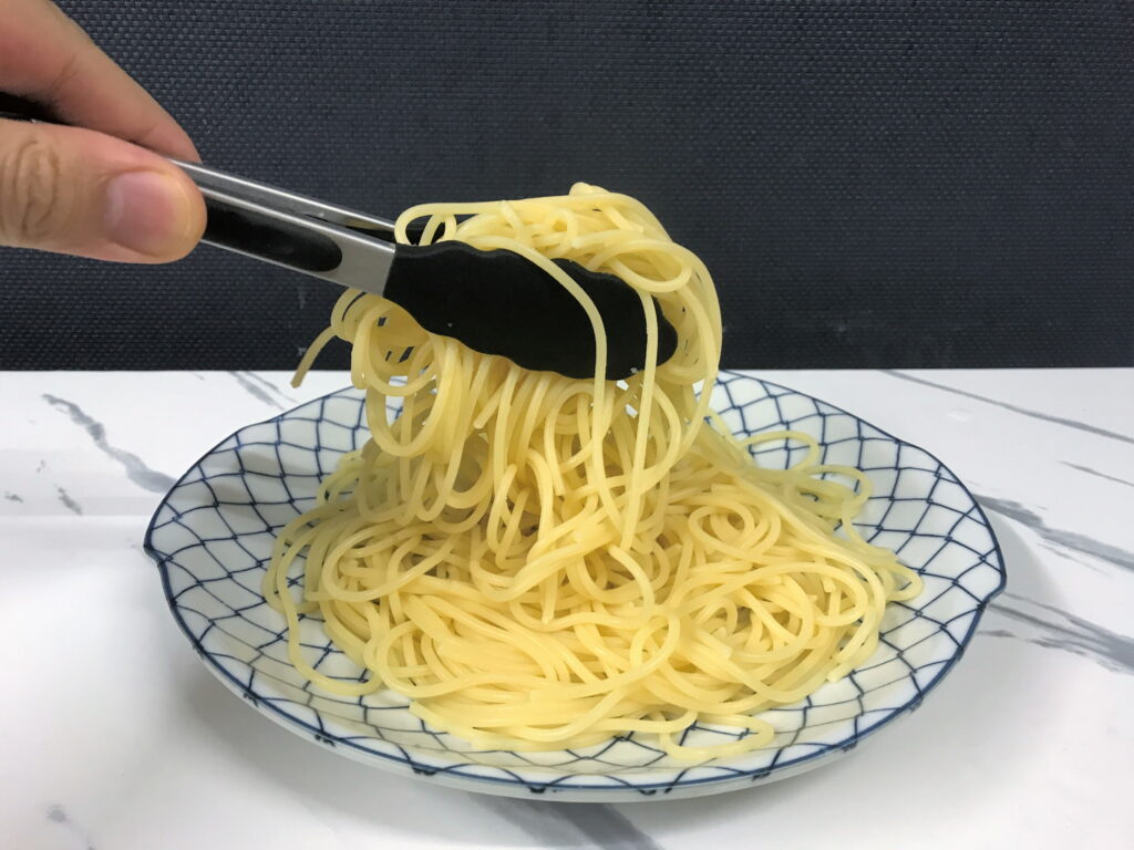 トングを使って茹でたスパゲッティを盛り付ける