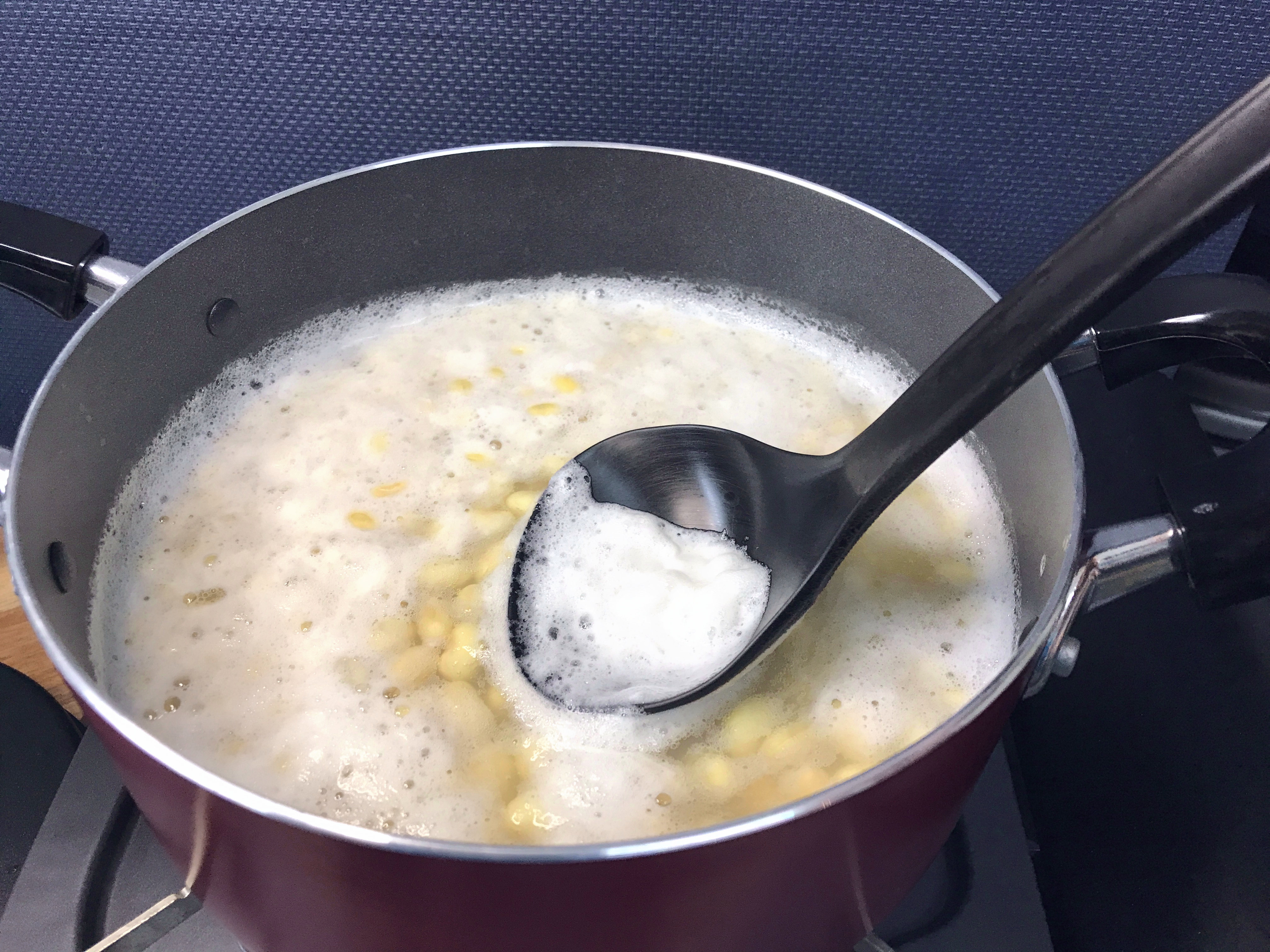 水で戻した大豆を鍋で茹でながらおたまを使ってアク取り